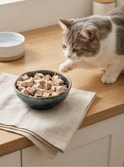 PawDry Freeze-Dried Duck Bites Pets Treats 100g in a bowl with a cat approaching on a kitchen counter.