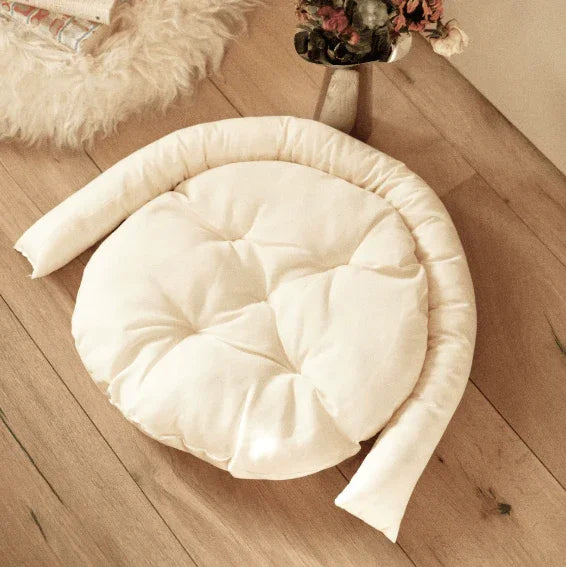 Cream round pet bed with bolster, cozy for cats and dogs on wooden floor