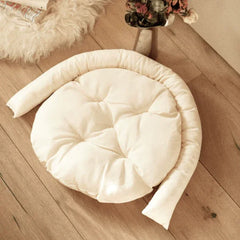 Cream round pet bed with bolster, cozy for cats and dogs on wooden floor