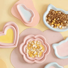 Cute pastel pet bowls in heart, flower, and cat ear shapes filled with dry dog or cat food, perfect for stylish pet feeding.
