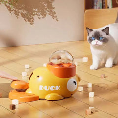 Yellow duck-shaped cat puzzle feeder with treat dispenser, engaging curious cat on wooden floor