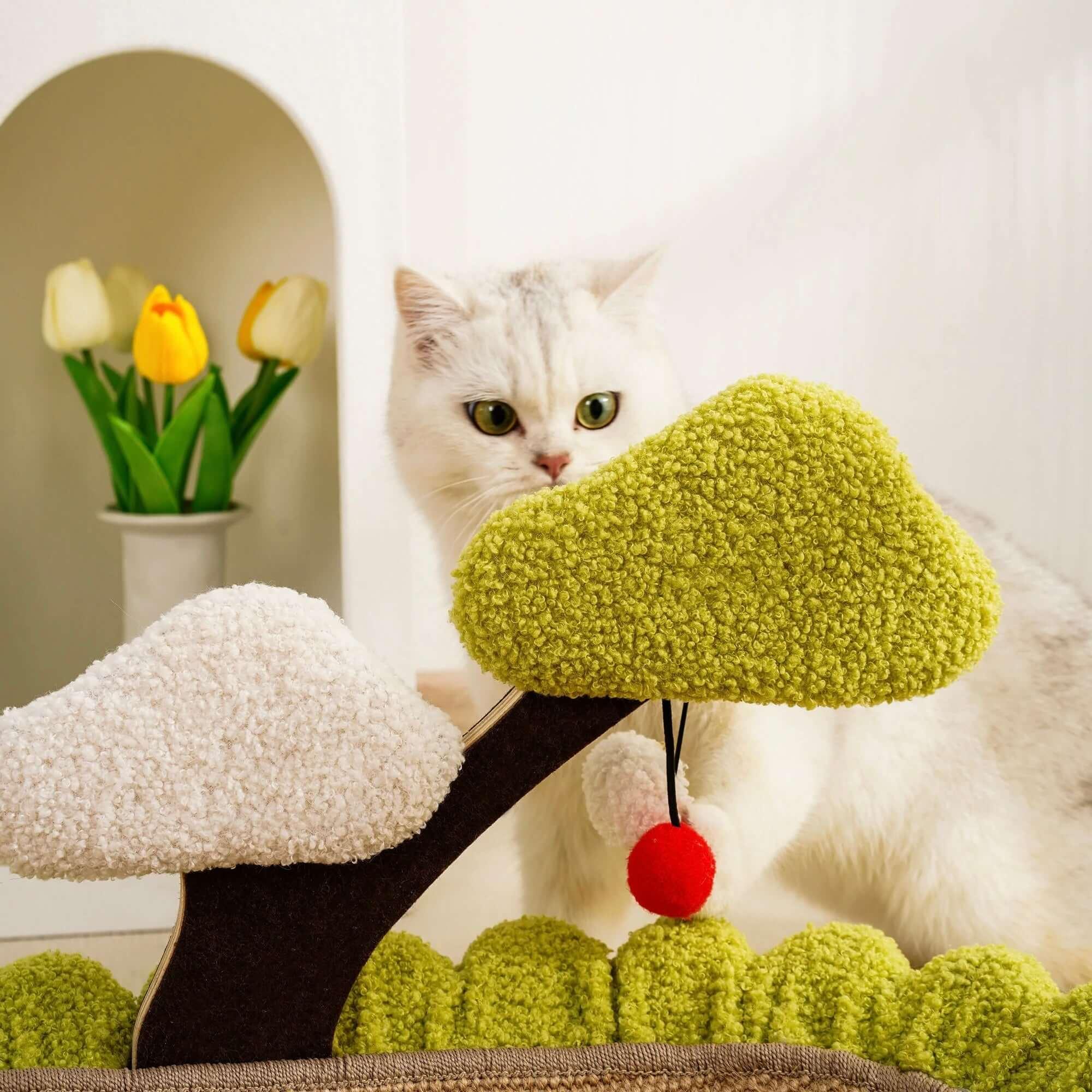 White cat playing with green and white textured cat tree toy featuring red pom-pom, ideal for indoor feline fun.
