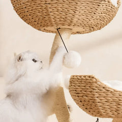 Fluffy white cat playing with pom-pom toy on woven wicker cat tree with scratching post