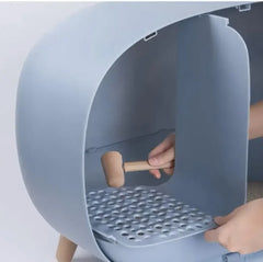 Modern gray cat litter box with wooden legs and perforated tray, being assembled by hand