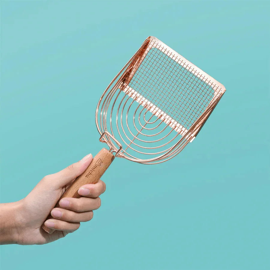 Stainless Steel Cat Litter Scoop Michu - 2 Styles held in a hand with a rose gold finish against a teal background.