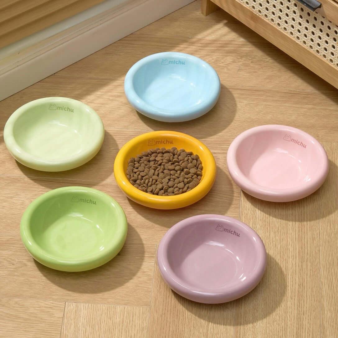 Colorful Michu pet bowls for cats and dogs, one filled with dry food, on wooden floor