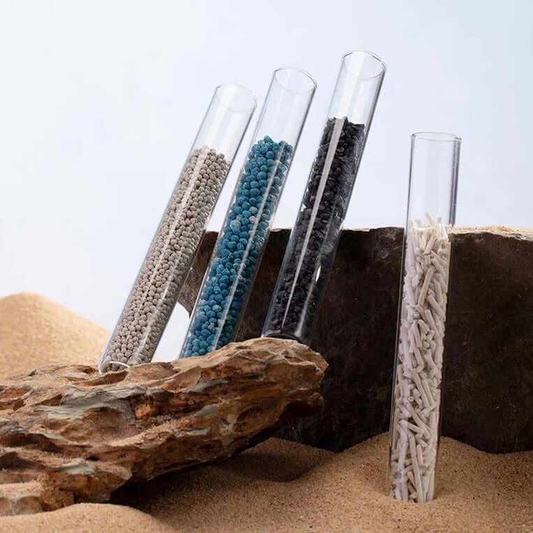 Colorful cat litter granules in glass tubes on sandy rocks, showcasing pet supplies for cats
