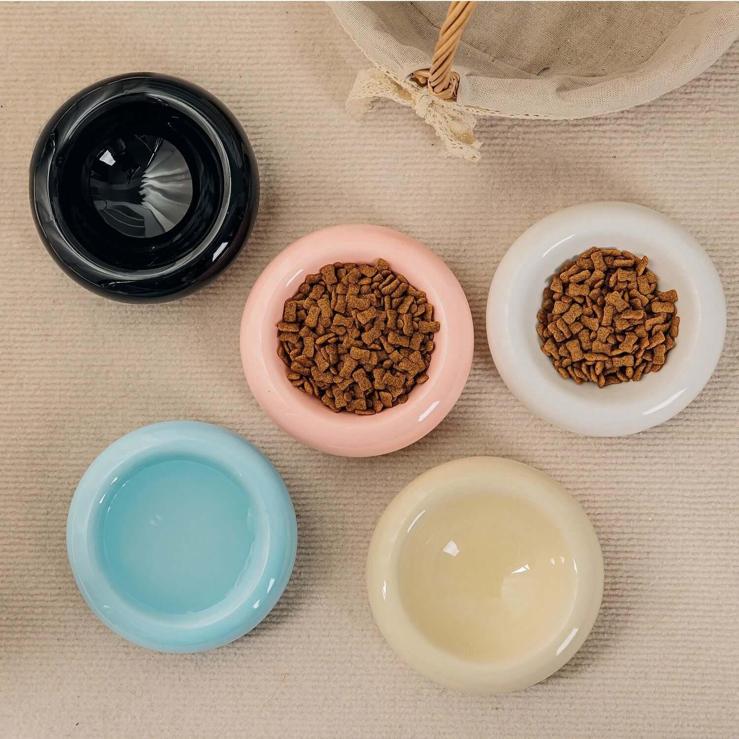 Stylish ceramic pet bowls in black, pink, white, blue, and cream, filled with dry food and water for cats and dogs.