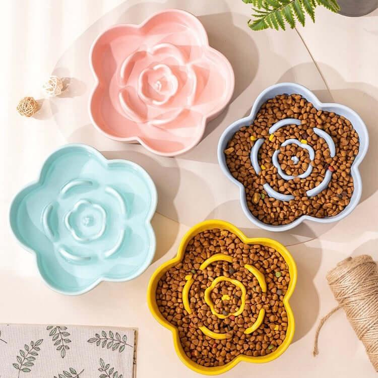 Flower-shaped slow feed dog bowls in pink, blue, and yellow with kibble, styled for pet feeding