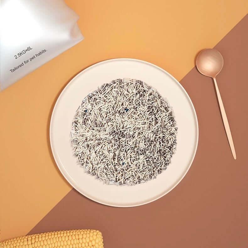 White and gray pet litter granules on plate with corn cob, spoon, and bag labeled 2.5KG=6L