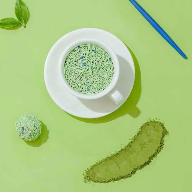 Matcha green tea powder in white cup with saucer, loose powder, and tea ball on green background