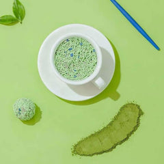 Matcha green tea powder in white cup with saucer, loose powder, and tea ball on green background