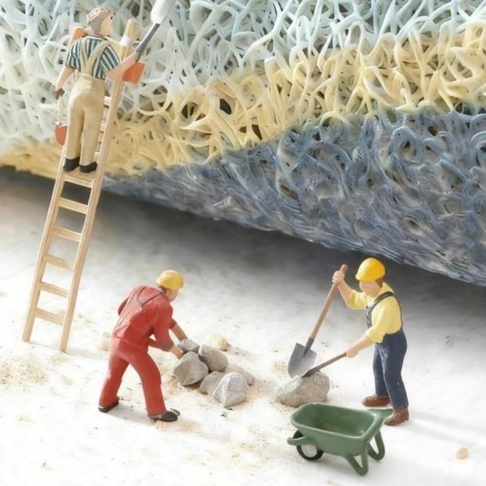 Miniature figurines working on a textured surface, depicting a construction scene with a ladder and wheelbarrow.