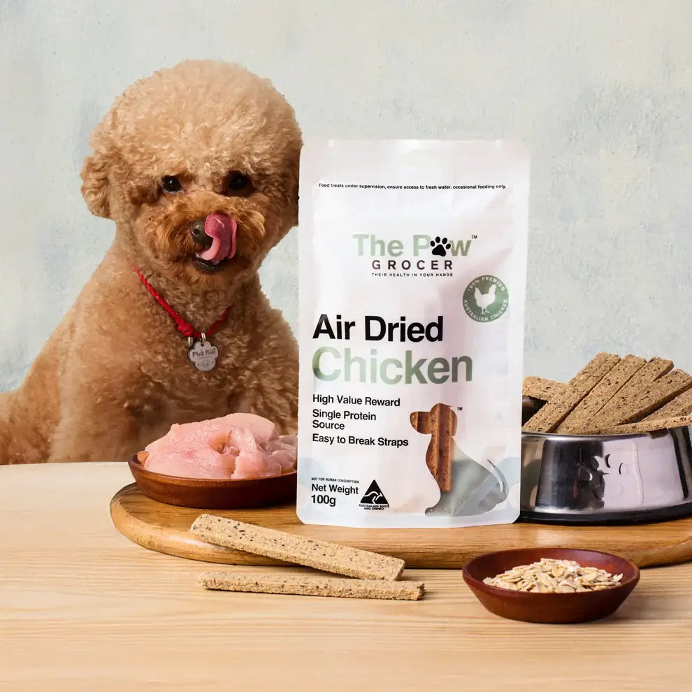 THE PAW GROCER Air-Dried Chicken Dog Training Straps 100g with a dog and treats on a wooden surface.