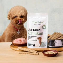 THE PAW GROCER Air-Dried Chicken Dog Training Straps 100g with a dog and treats on a wooden surface.