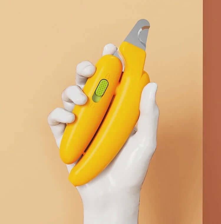 Yellow banana-shaped pet nail clipper with green safety guard, held in white hand against warm background