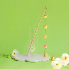 Cat wand toy with pink handle and flower pom-poms on green background, ideal for playful cats