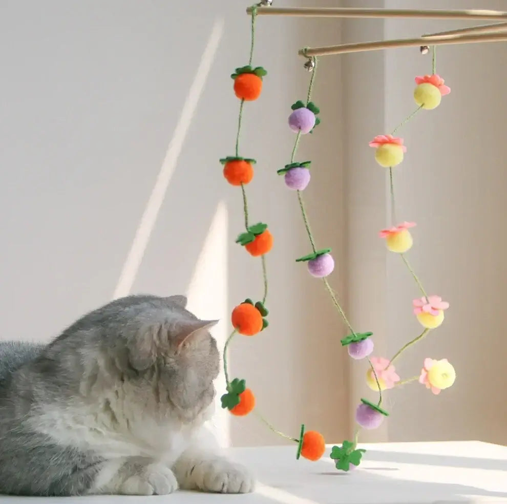 Grey cat playing with colorful felt fruit and flower cat toy hanging from wooden frame