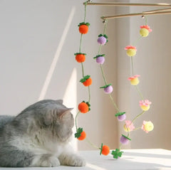Grey cat playing with colorful felt fruit and flower cat toy hanging from wooden frame