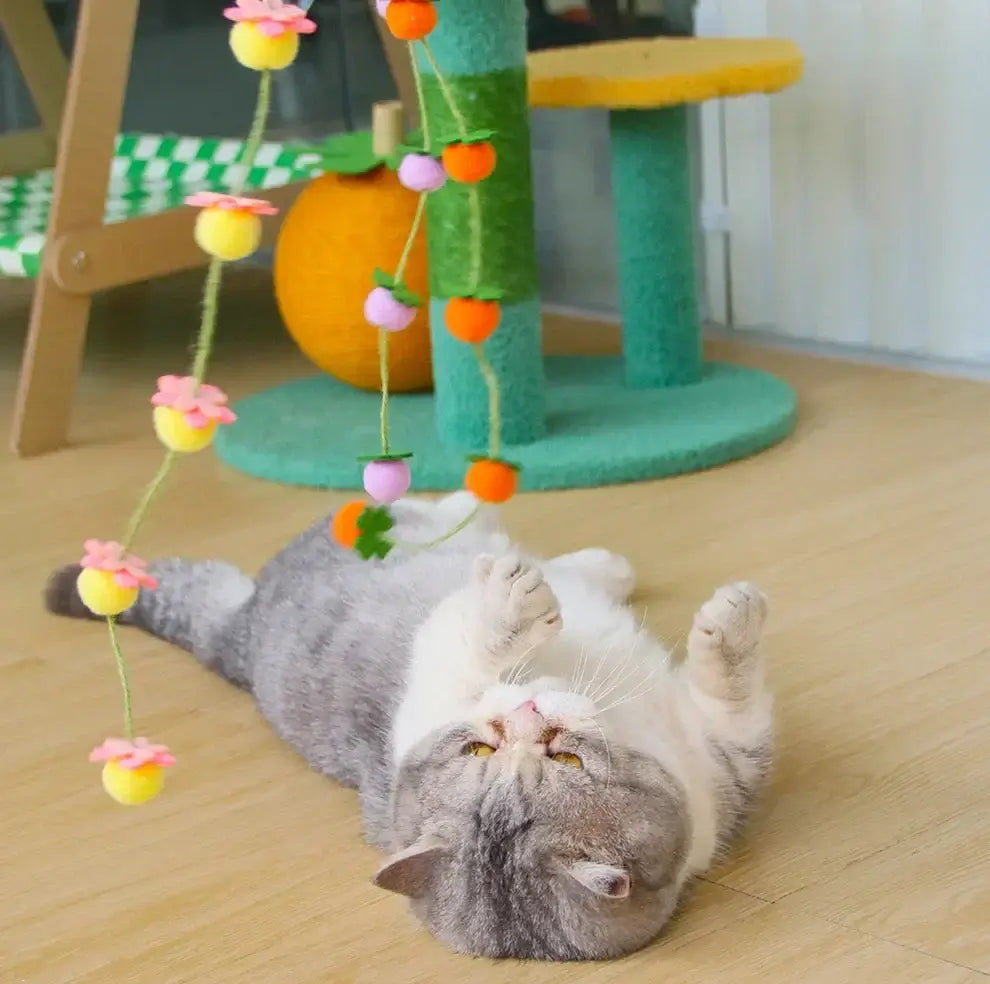 Gray cat playing with colorful hanging toy near green cat tree, perfect for indoor pet fun and enrichment