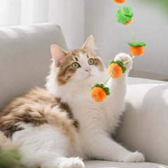 Fluffy cat playing with orange pom-pom toy on string, perfect for indoor cat entertainment and exercise.