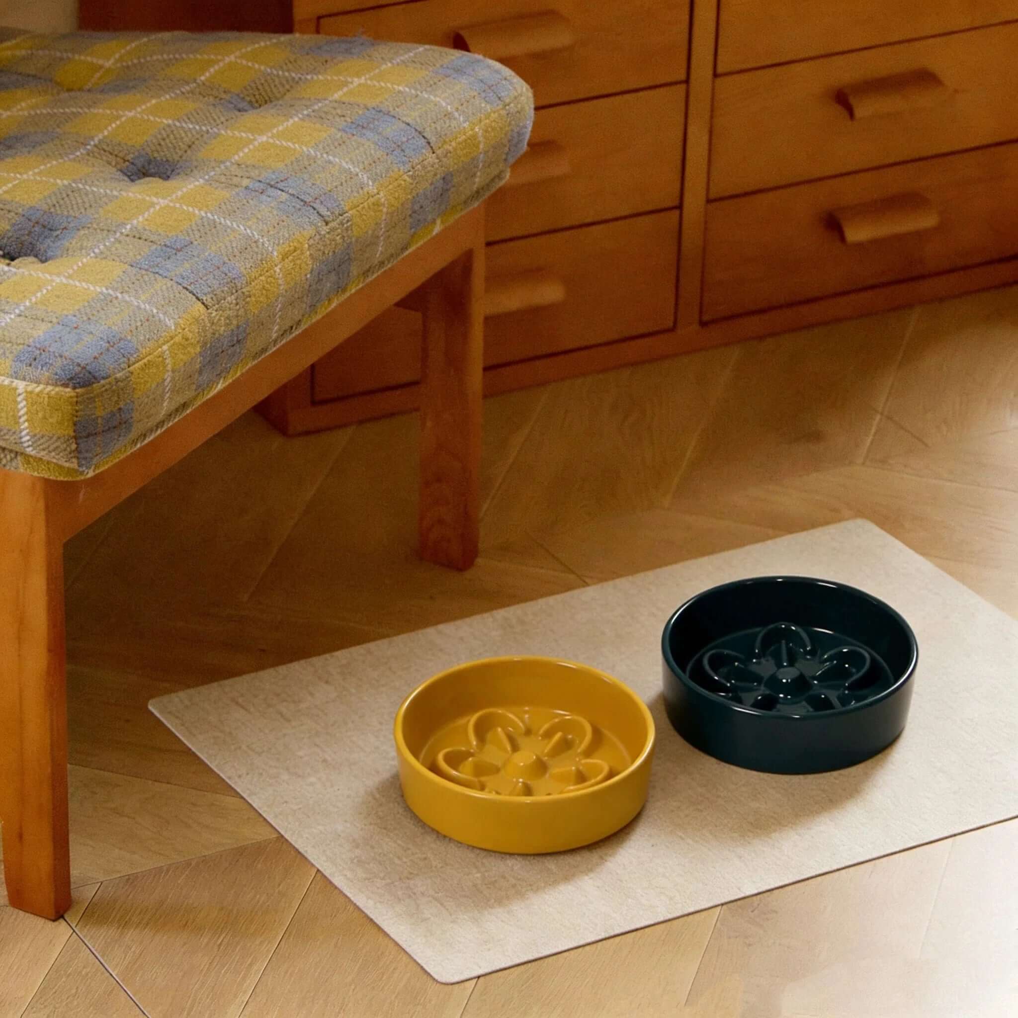 Yellow and navy slow feeder dog bowls on mat under wooden bench, stylish pet supplies for home